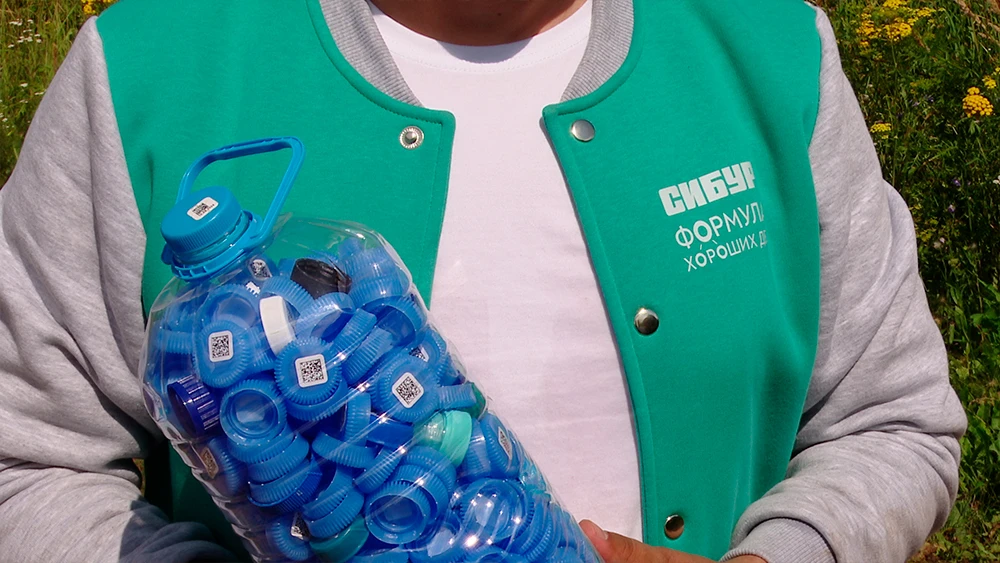 Пластиковые крышки в бутылке на фоне человека в куртке с надписью СИБУР