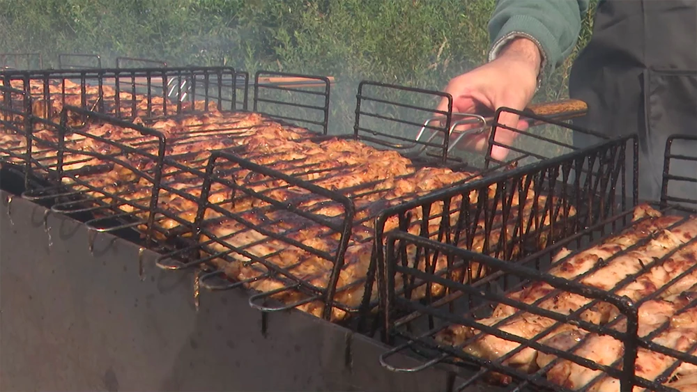 Мужчина жарит шашлык на мангале, куски мяса лежат на решетке