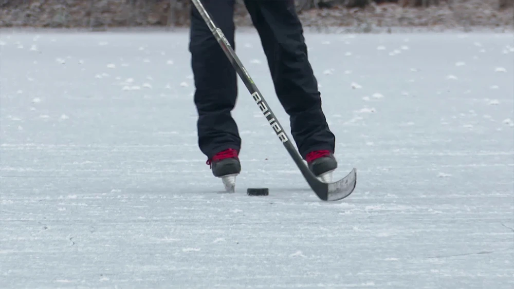 Человек катается на коньках по льду с клюшкой
