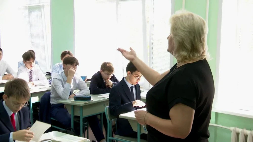 учитель в классе ведет урок в старших классах, за партами сидят ученики