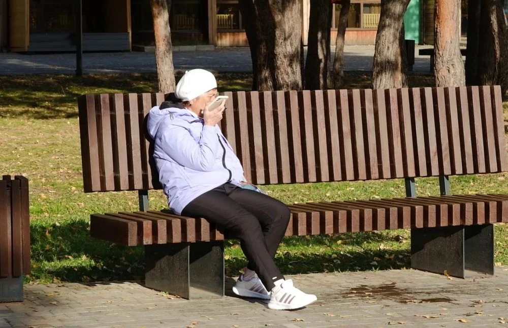 пенсионерка сидит на скамейке и разговаривает по телефону
