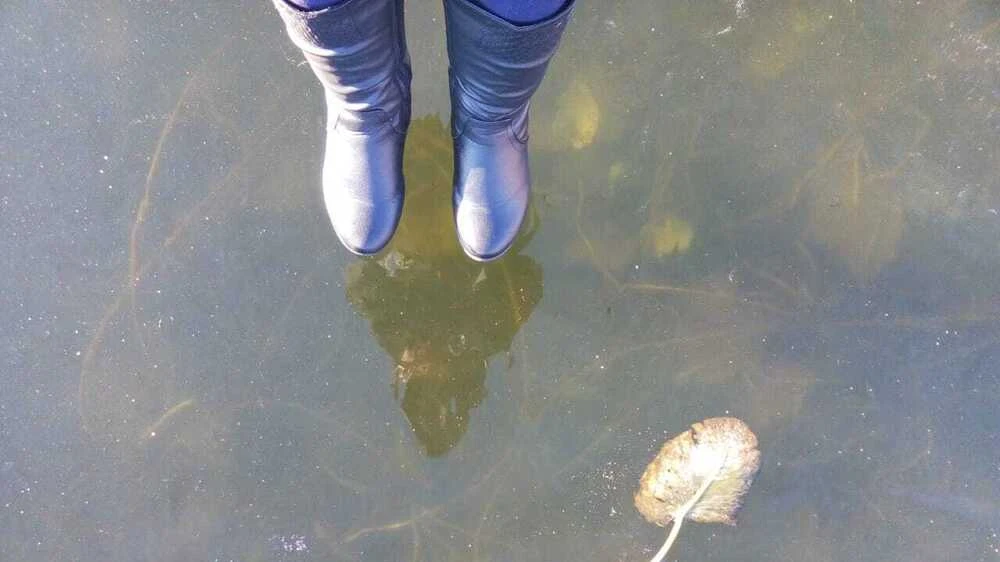 Женщина стоит в сапогах на тонком льду
