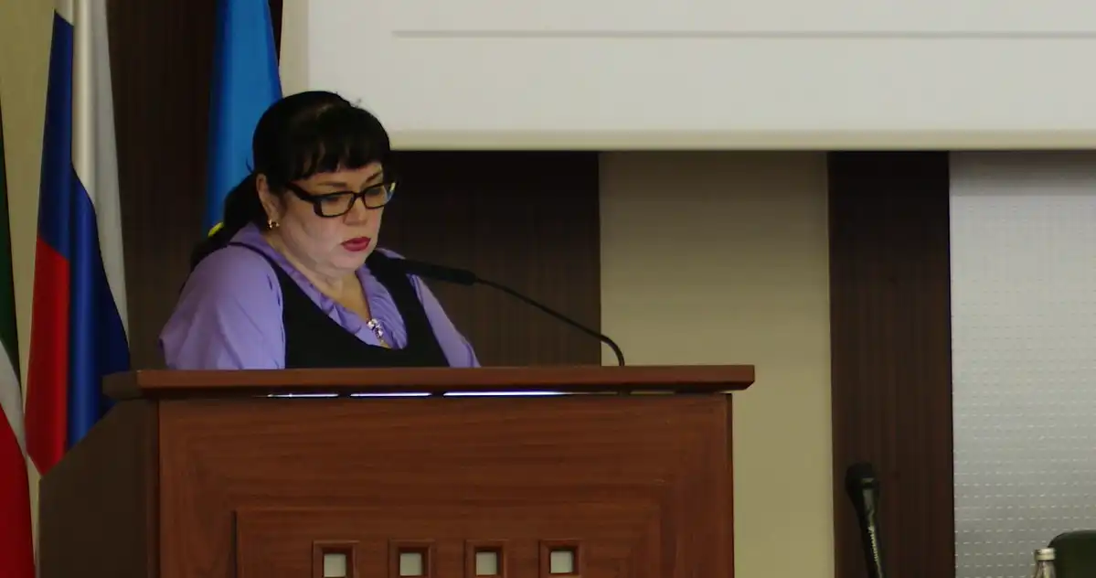 Женщина стоит за трибуной и говорит в микрофон