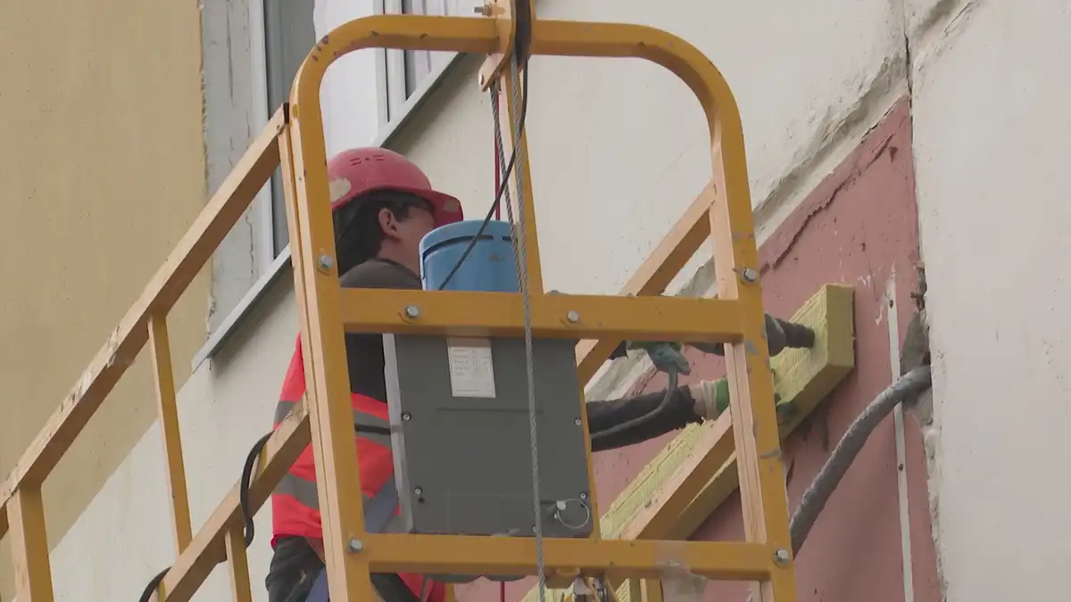 Рабочий в строительной люльке ремонтируют фасад дома