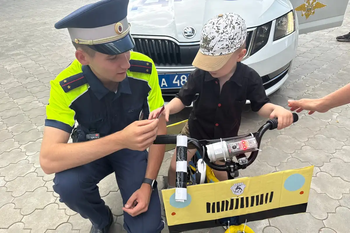 полицейский разговаривает с ребенком на параде детского транспорта