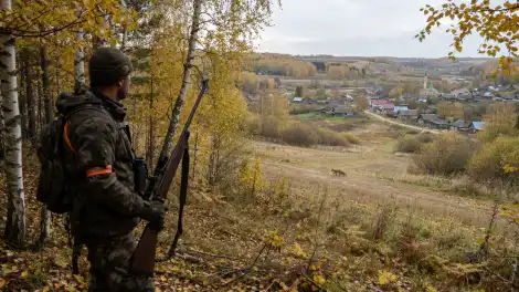 охотник стоит ружьем у леса